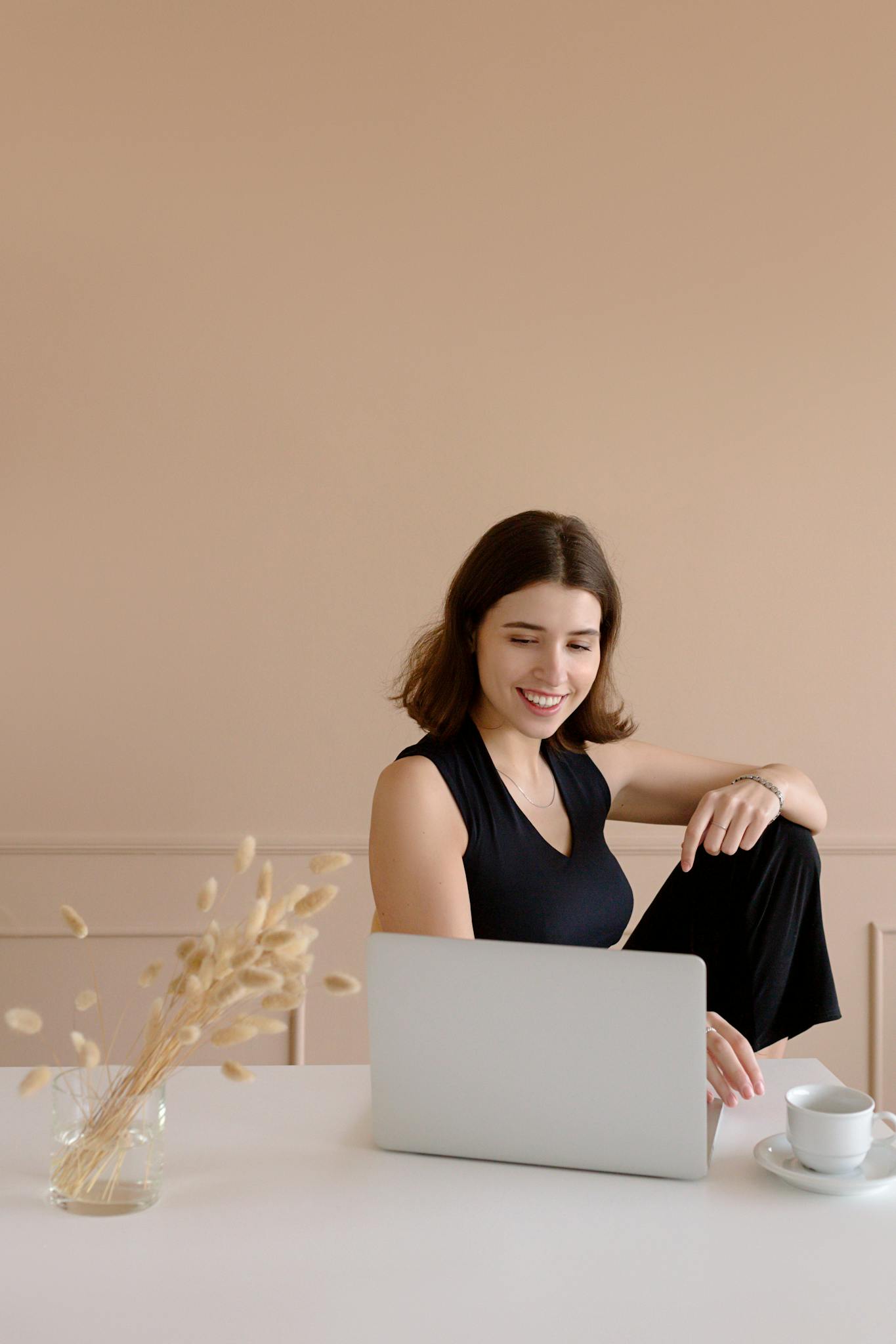A cheerful woman works on her laptop at home, enjoying a relaxed lifestyle.