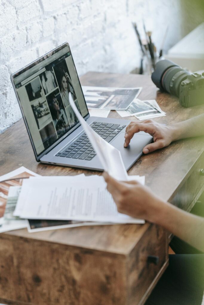 Photographer reviewing images on a laptop and working with documents in a creative workspace.